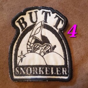 Puede incluir: Parche bordado en blanco y negro con el texto "Butt Snorkeler" y una imagen de dibujos animados de una persona con un snorkel y equipo de buceo.