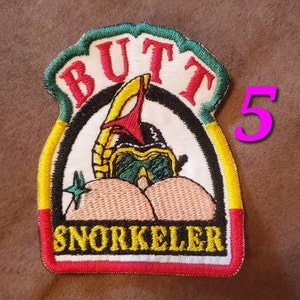Puede incluir: Un parche bordado colorido con las palabras "Butt Snorkeler" y una imagen de dibujos animados de una persona con un snorkel y gafas de buceo. El parche es amarillo, verde, rojo y blanco.