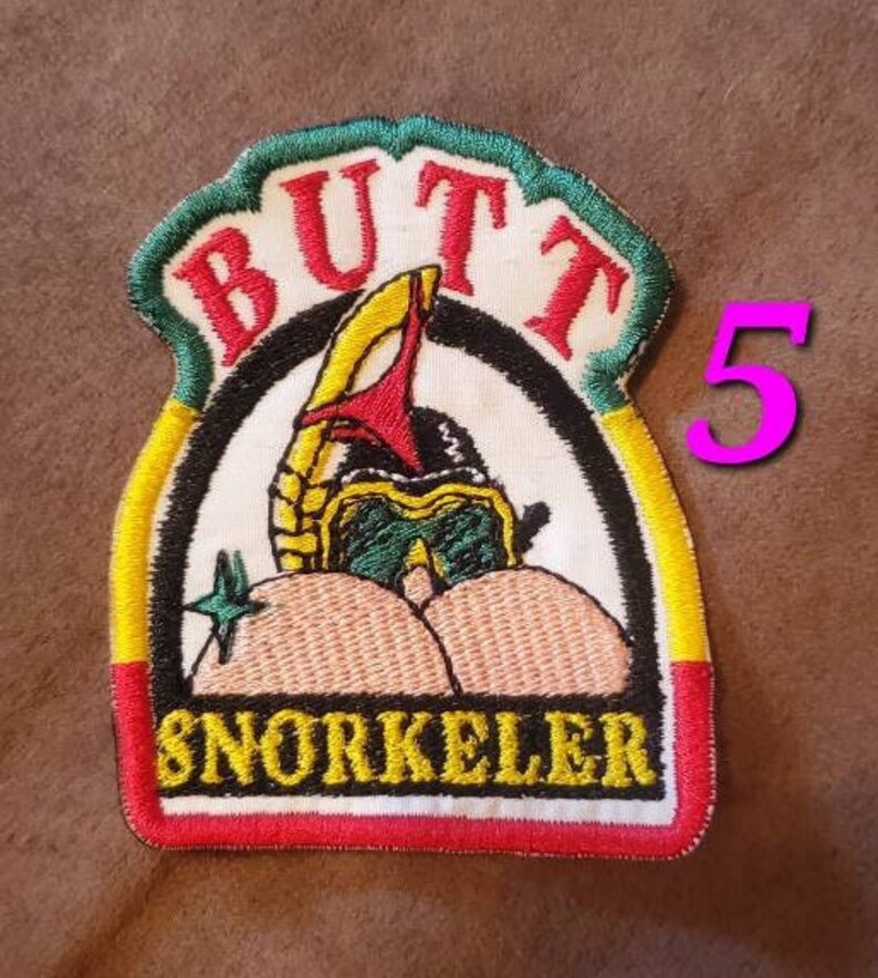 Puede incluir: Un parche bordado colorido con las palabras "Butt Snorkeler" y una imagen de dibujos animados de una persona con un snorkel y gafas de buceo. El parche es amarillo, verde, rojo y blanco.
