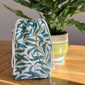 May include: A white drawstring bag with a teal floral pattern. The bag is made of fabric and has a white drawstring closure.