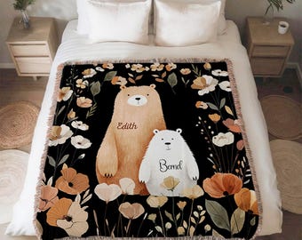 May include: A black throw blanket featuring two bears and floral designs. One bear is tan, the other is white. The names "Edith" and "Bernd" are printed on the bears. The blanket is fringed.