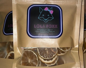 Pode incluir: Saco de papel castanho com uma janela transparente contendo fatias de limão secas. O saco tem um rótulo com o texto "LOLA FOXX" e um logotipo de raposa. O rótulo na parte inferior diz "LIMON 2OZ BB092523".