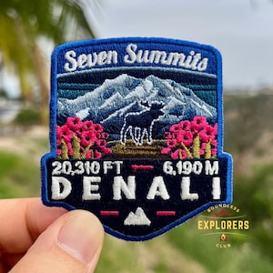 May include: Embroidered patch with a blue border featuring the text "Seven Summits" and "Denali." The patch depicts a mountain range, a moose silhouette, and pink flowers. Measurements are listed as 20,310 FT and 6,190 M. The patch also includes the text "Boundless Explorers Club."