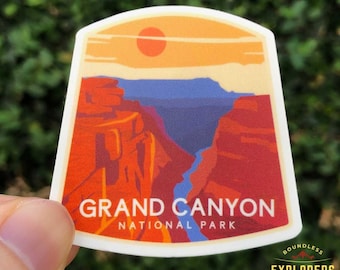 Op de afbeelding: Een sticker met een retro-illustratie van het Grand Canyon National Park. De sticker heeft een rood-oranje-blauwe kleurstelling en toont een zonsondergang boven de canyon. De tekst "Grand Canyon National Park" is in wit op de sticker gedrukt. De sticker heeft ook een klein logo in de rechterbenedenhoek dat "Boundless Explorers Club" zegt.