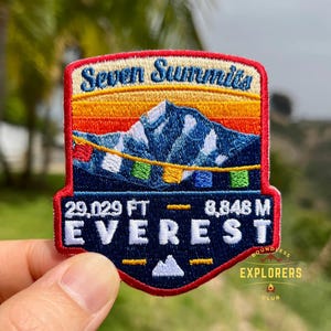 Könnte beinhalten: Gestickter Aufnäher mit einer Berglandschaft, dem Text "Seven Summits" und "Everest". Der Aufnäher zeigt die Höhe in Fuß und Metern: 29.029 FT - 8.848 M. Das Design beinhaltet einen Sonnenuntergang und farbenfrohe Gebetsfahnen.
