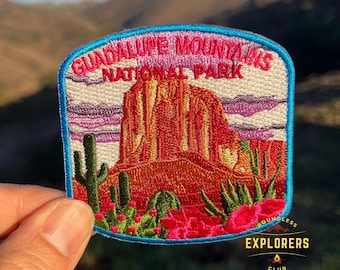 May include: Embroidered patch featuring a colorful depiction of Guadalupe Mountains National Park, with a mountain range, cacti, and a sunset sky. The patch has a blue border and the text "Guadalupe Mountains National Park" in white.