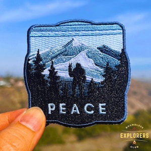 May include: A blue and black embroidered patch featuring a silhouette of Bigfoot standing in front of a mountain range. The patch reads "PEACE" in white lettering.