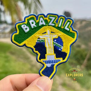 May include: Embroidered patch featuring the shape of Brazil with the word "BRAZIL" in white letters. The patch includes the Christ the Redeemer statue, and the colors of the Brazilian flag: green, yellow, and blue. The patch is outlined in blue and yellow.