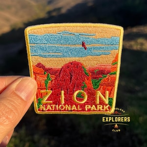 Peut inclure: Un écusson brodé jaune avec les mots "Zion National Park" et une représentation d'une formation rocheuse rouge avec un ciel bleu au-dessus. L'écusson a une bordure jaune et les mots "Endless Explorers Club" sont imprimés en dessous.
