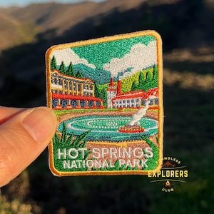 May include: A colorful embroidered patch featuring a vintage illustration of Hot Springs National Park, with a building, a pool of water, and green trees. The text "Hot Springs National Park" is embroidered in white on a green background. The patch is surrounded by a gold border and has the text "Boundless Explorers Club" in the bottom right corner.