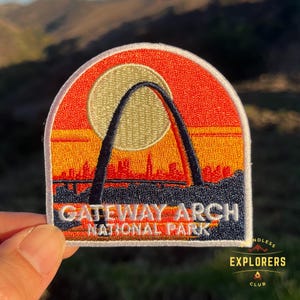 May include: A white, red, and yellow embroidered patch with an image of the Gateway Arch in St. Louis, Missouri. The text "Gateway Arch National Park" is below the arch.