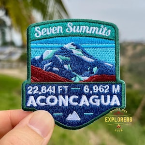 May include: Embroidered patch featuring the text "Seven Summits" above a mountain scene in blue, green, and red. The patch includes the text "22,841 FT - 6,962 M ACONCAGUA" and "Boundless Explorers Club".