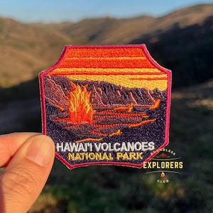 May include: An embroidered patch featuring a volcano erupting, in shades of red, yellow and purple. The patch reads "Hawaii Volcanoes National Park" and "Boundless Explorers Club".