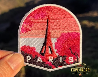 Può includere: Toppa ricamata da stirare con una scena di tramonto rosa e rosso con la Torre Eiffel al centro. Il testo "PARIS" è sotto la torre. La toppa ha un bordo bianco e uno sfondo bianco. Il testo "EXPLORERS CLUB" è nell'angolo in basso a destra.