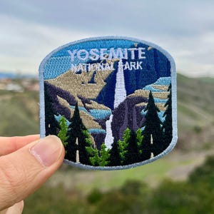 May include: A blue and white embroidered patch featuring the text "Yosemite National Park" and an image of a waterfall and trees.