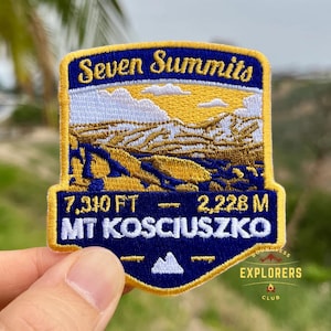 May include: Embroidered patch with the text "Seven Summits" and "Mt Kosciuszko". The patch features a mountain landscape in shades of gold, brown, and blue. The patch also includes the height of the mountain in feet and metres.