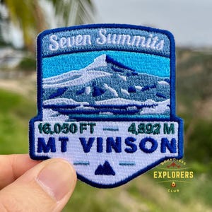 May include: Embroidered patch featuring a mountain landscape with the text "Seven Summits" and "Mt Vinson". The patch includes the elevation in feet and meters, and the text "Boundless Explorers Club". The patch is blue and white.