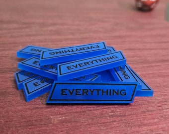 May include: A pile of blue game tokens with the word "EVERYTHING" printed in black. The tokens are rectangular with a black border. The background is a reddish-brown wooden surface.