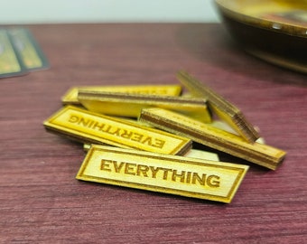May include: A close-up of several small, rectangular wooden game pieces. Each piece is engraved with the word "EVERYTHING" in a bold, sans-serif font. The pieces are light brown with darker brown edges.