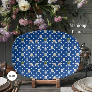May include: An oval-shaped platter with a deep blue background featuring a white polka dot pattern and repeating illustrations of mahjong tiles, blue and white ginger jars, fans, and topiary plants. The platter is labeled Mahjong Platter.