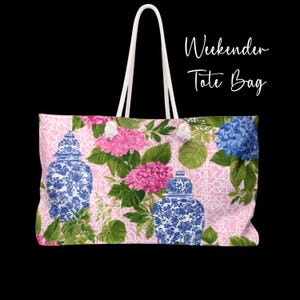 May include: Pink tote bag with a floral pattern featuring blue and white decorative jars, pink and blue hydrangeas, and green leaves. The bag has white rope handles and the text "Weekender Tote Bag" in white script.