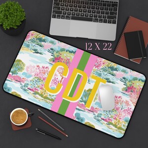 May include: A rectangular desk mat featuring a colorful floral landscape pattern with a central vertical pink and green stripe. The letters CDT are printed in large yellow font across the center. The mat measures 12 inches by 22 inches.