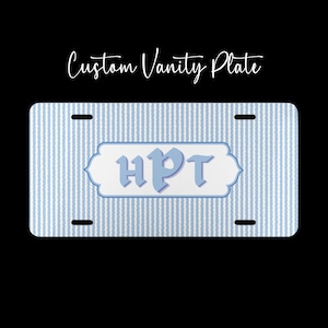 May include: Custom vanity plate with a blue and white striped background. The plate features the letters "HPT" in a light blue color within a white and blue decorative frame. The text "Custom Vanity Plate" is written in cursive.