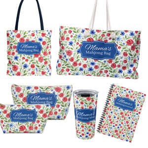 May include: A collection of floral-patterned accessories, including tote bags, cosmetic bags, a tumbler, and a journal. Each item features a design of red roses, blue flowers, and green leaves on a white background. The text "Mama's Mahjong Bag" and "Mama's Mahjong Journal" are displayed.