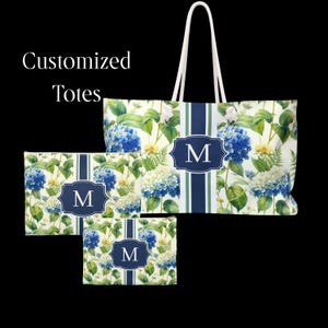 May include: A large tote bag and two smaller pouches featuring a floral pattern of blue and white hydrangeas with green leaves. Each item has a central vertical navy blue stripe and a navy blue rectangular emblem with the white letter M.