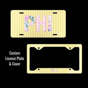 May include: A rectangular license plate featuring a yellow and white vertical striped background with the letters PHI in floral and pink gingham patterns, alongside a matching license plate frame with the same yellow and white striped design.