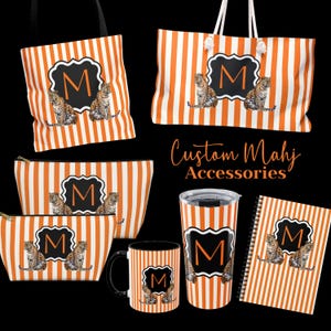 May include: A collection of custom accessories featuring an orange and white striped pattern. The items include tote bags, cosmetic bags, a tumbler, a mug, and a notebook. Each item has a black and white emblem with the letter "M" and a leopard illustration.