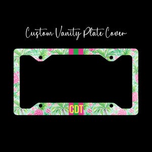 May include: A rectangular vanity plate cover featuring a tropical pattern of green palm leaves and pink pineapples. A vertical pink and green stripe runs through the center, with the yellow letters CDT printed on the bottom. Text reads Custom Vanity Plate Cover.