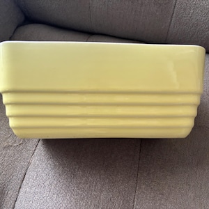 May include: A rectangular, pale yellow ceramic baking dish. The dish has a series of horizontal ridges on the lower half of its exterior. The overall shape is a simple, yet elegant design, suitable for baking and serving.