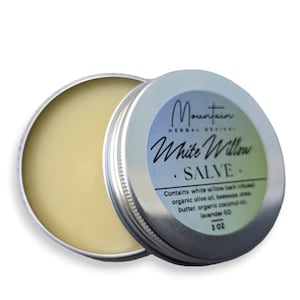May include: A silver tin with a white label that reads "Mountain Herbal Rejuvenu White Willow Salve". The label also includes the ingredients: white willow bark infused organic olive oil, beeswax, shea butter, organic coconut oil, lavender EO. The tin contains a yellow salve and is labeled 2 oz.