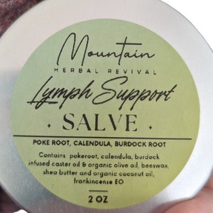 May include: A silver tin with a green label that reads "Mountain Herbal Revival Lymph Support Salve". The label also lists the ingredients: "Poke Root, Calendula, Burdock Root". It also says "Contains pokeroot, calendula, burdock infused caster oil & organic olive oil, beeswax, shea butter and organic coconut oil, frankincense EO". The label also says "2 OZ".