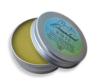 May include: A silver tin with a green and blue label that reads "Dreamland SALVE" and lists the ingredients: mugwort, passionflower, chamomile, lavender flower, beeswax, shea butter, organic olive oil, organic coconut oil, Lavender EO & Vetiver EO. The tin is open and a yellow salve is visible inside. The tin is 2 oz.