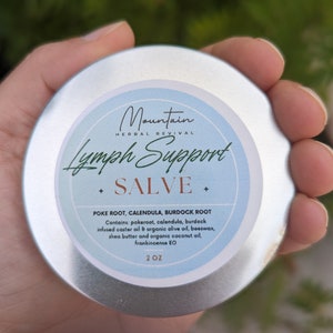 May include: A silver tin of Mountain Herbal Revival Lymph Support Salve, with a blue label and white text. The label reads "Lymph Support Salve" and lists the ingredients: Poke Root, Calendula, Burdock Root. It also lists the ingredients: pokeroot, calendula, burdock infused caster oil & organic olive oil, beeswax, shea butter and organic coconut oil, frankincense EO. The tin is 2 oz.