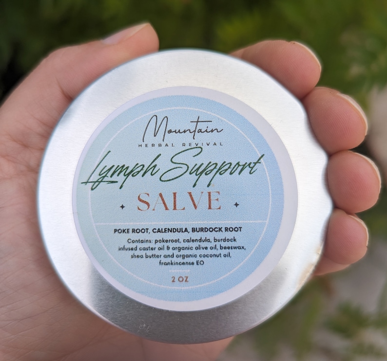 May include: A silver tin of Mountain Herbal Revival Lymph Support Salve, with a blue label and white text. The label reads "Lymph Support Salve" and lists the ingredients: Poke Root, Calendula, Burdock Root. It also lists the ingredients: pokeroot, calendula, burdock infused caster oil & organic olive oil, beeswax, shea butter and organic coconut oil, frankincense EO. The tin is 2 oz.