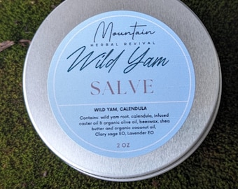 May include: A silver tin with a blue label that reads "Mountain Herbal Revival Wild Yam Salve". The label also lists the ingredients: "Wild Yam, Calendula" and "Contains: wild yam root, calendula, infused caster oil & organic olive oil, beeswax, shea butter and organic coconut oil, Clary sage EO, Lavender EO". The tin is labeled "2 OZ".