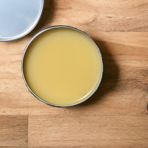 May include: A round metal tin with a lid, filled with a yellow balm or ointment.
