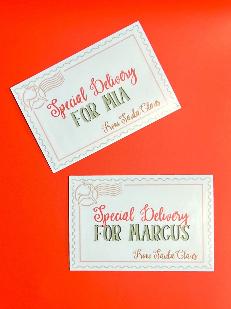 K&ouml;nnte beinhalten: Zwei wei&szlig;e Geschenkanh&auml;nger mit einem Rentier-Motiv und dem Text "Special Delivery" in Rot. Der erste Anh&auml;nger lautet "For Mia" und der zweite Anh&auml;nger lautet "For Marcus". Beide Anh&auml;nger tragen den Text "From Santa Claus" in einer kleineren Schriftart.