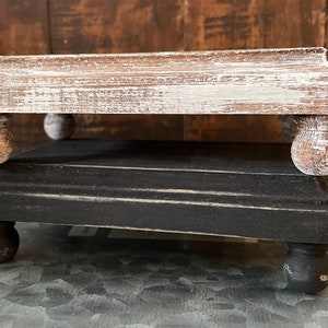 May include: Two wooden tiered risers, one whitewashed and one black. Both have rounded feet.