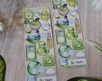 May include: Two sticker sheets with green and yellow graphics, including apples, globes, and cloud shapes. The text "Frutiger Eco" appears at the top of each sheet, and the word "Yeah!" is at the bottom. The stickers are on a wooden surface.