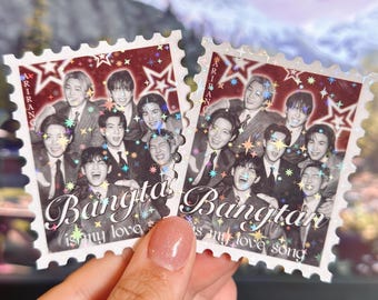 May include: Two postage stamp-shaped stickers featuring a group of people in suits. The stickers have a burgundy background with star and glitter accents. The text "Bangta is my love song" is written on the stickers.