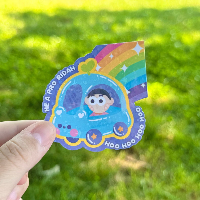 May include: A blue cartoon car with a rainbow and stars. The car has a smiling face and the text "HE A PRO RIDAH" and "HOO HOO HOO" around it. A cartoon character with brown hair is driving the car.