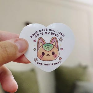 May include: A heart-shaped sticker with a cartoon animal face and the text "Some days all I can do is my best and that's okay." The sticker features a light brown animal face with a green leaf and pink accents.