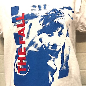 May include: White t-shirt with a blue and red graphic print of a man's face and the text "THE FALL" in red.