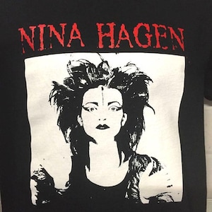 May include: Black t-shirt featuring a white image of Nina Hagen, a singer, with the text "NINA HAGEN" in red letters above the image.
