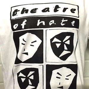 May include: White t-shirt with a black and white graphic. The graphic reads "theatre of hate" above four stylized faces. Each face is in a black square with a white outline, each showing a different expression.