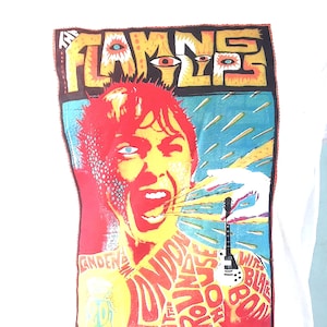 May include: White t-shirt featuring a colourful graphic print of a person singing into a microphone with a guitar. The graphic includes the text "The Flaming Lips" and "London Roundhouse".